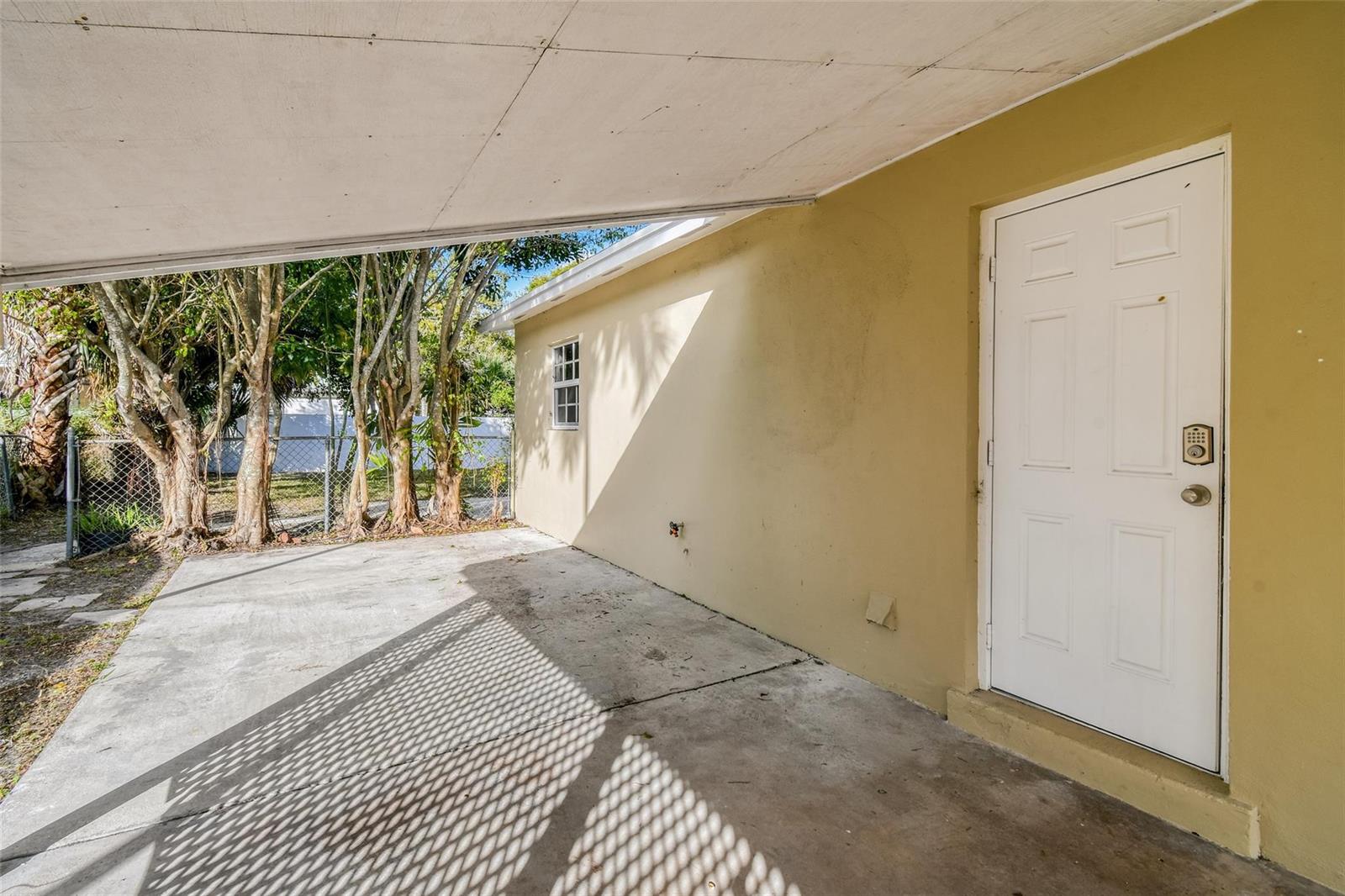 A concrete carport area features a white door with a keypad lock and a window — 1227 Cherokee Street, Jupiter FL 33458, JUPITER, FL