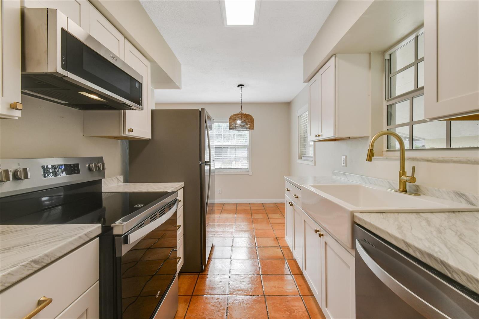 A kitchen features white cabinets, marble-look countertops, a farmhouse sink, and terracotta tile flooring — 1227 Cherokee Street, Jupiter FL 33458, JUPITER, FL