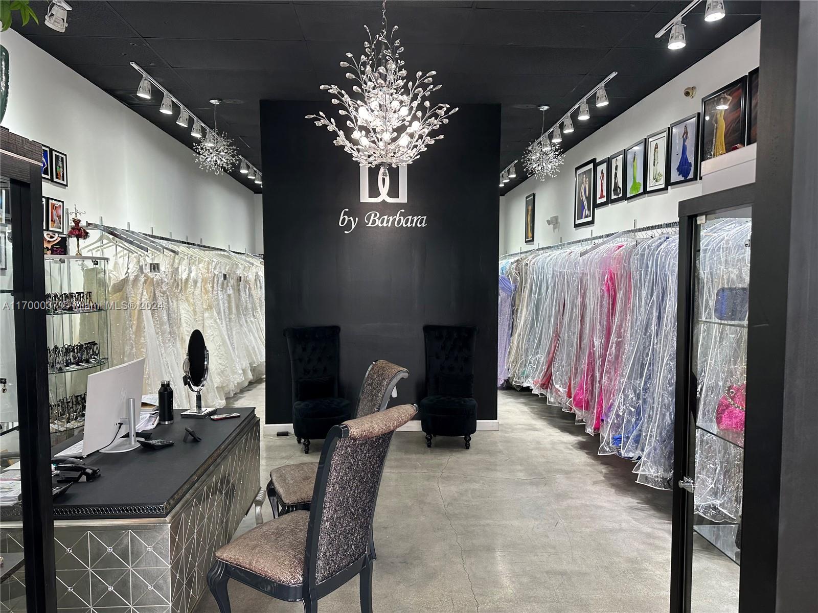 A boutique interior features rows of garment bags, black walls, and a central crystal chandelier — 14248 SW 8th St, Miami FL 33184, MIAMI, FL