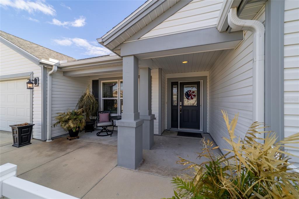 The exterior of a house features a covered front porch, gray siding, and a door — 1194 MCDONOUGH PLACE, THE VILLAGES, FL