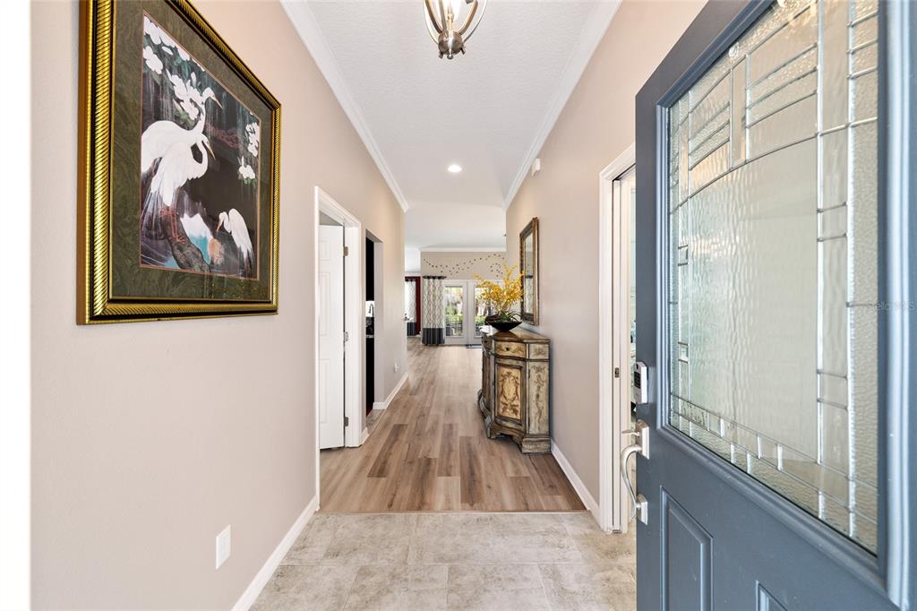 A foyer with tile flooring leads into a hallway with wood-look floors and a console table — 1194 MCDONOUGH PLACE, THE VILLAGES, FL