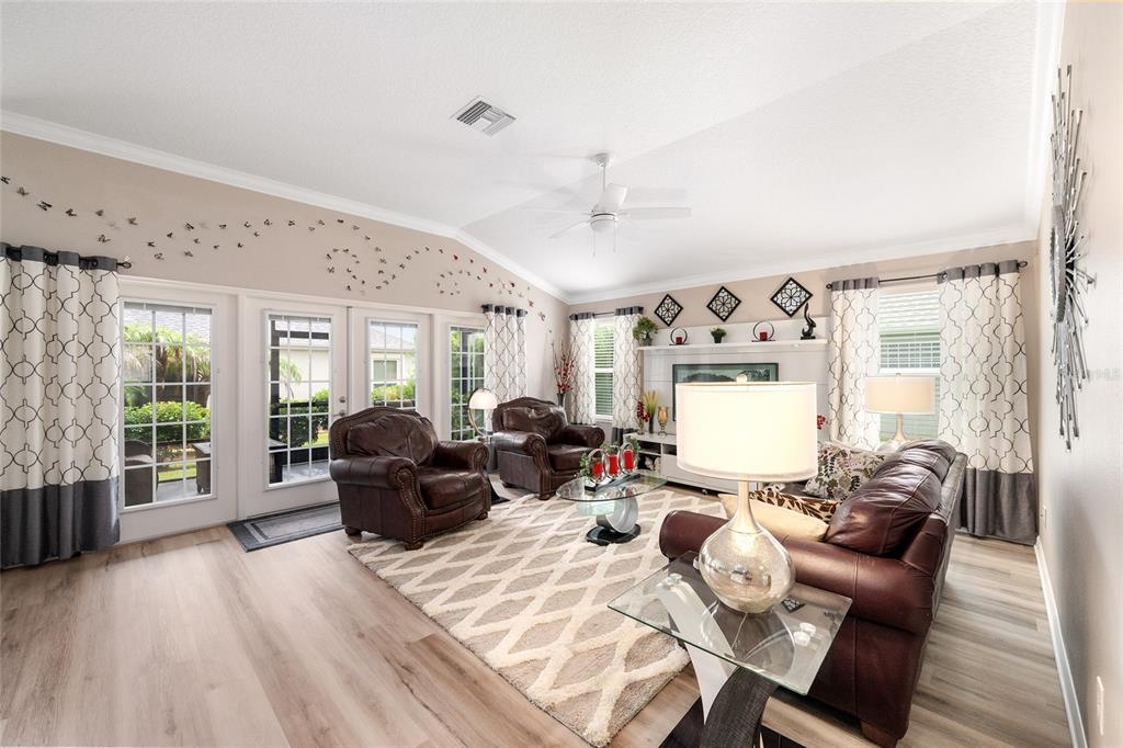 A living room features leather furniture, a patterned rug, and glass doors leading outside — 1194 MCDONOUGH PLACE, THE VILLAGES, FL