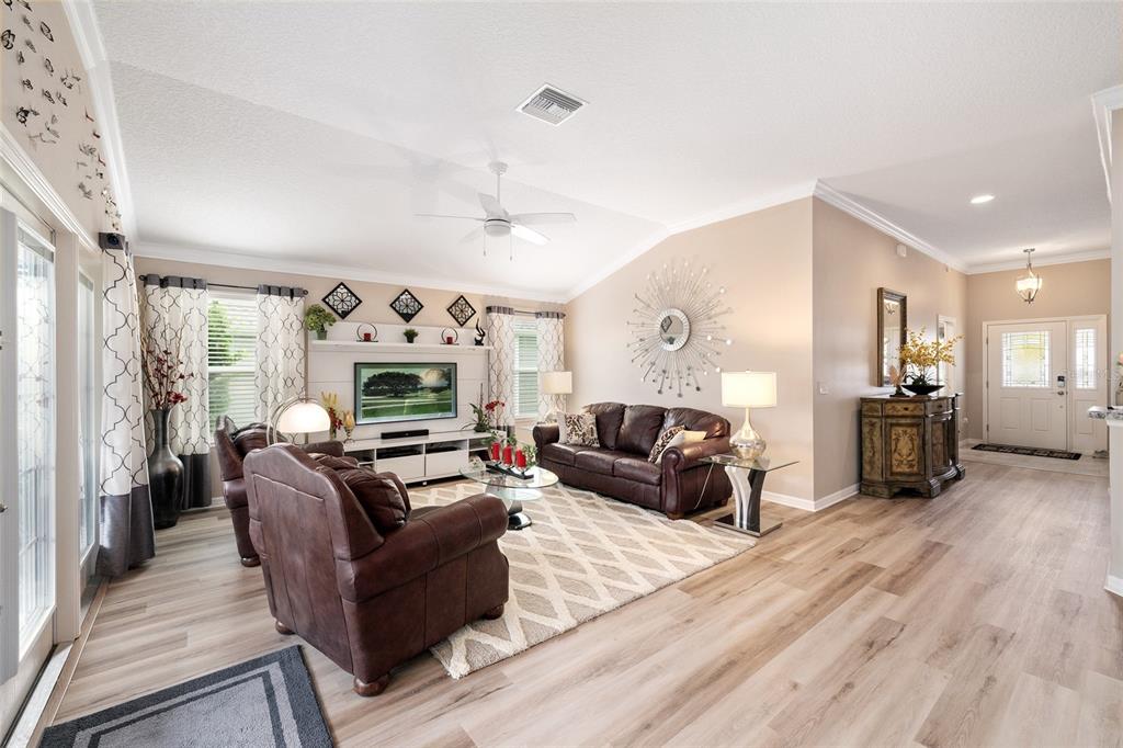 A living room features brown leather furniture, a white media console, and light wood flooring — 1194 MCDONOUGH PLACE, THE VILLAGES, FL
