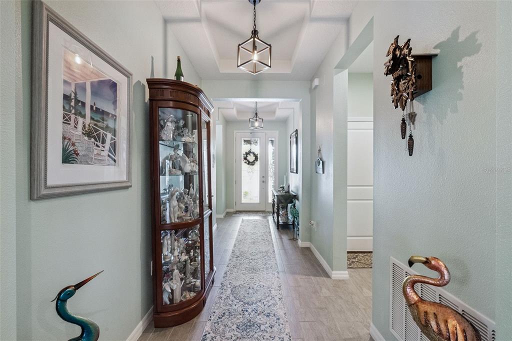 A hallway features light blue walls, wood-look tile flooring, a curio cabinet, and pendant lighting — 3904 REDFIN PLACE, KISSIMMEE, FL