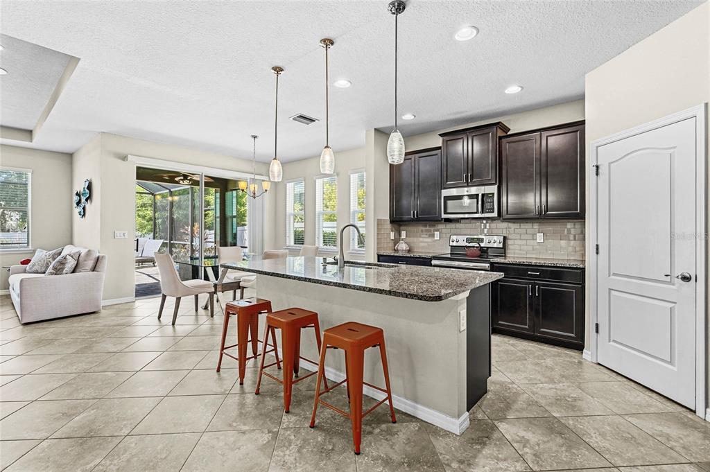 A kitchen features dark wood cabinets, granite countertops, an island with orange stools, and tile floors — 5309 CHARLIE BROWN LANE, SARASOTA, FL