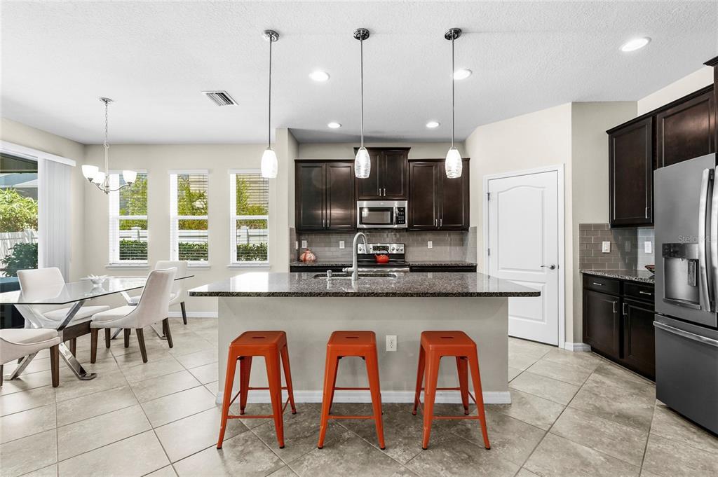 A kitchen features dark wood cabinets, granite countertops, an island with orange stools, and tile flooring — 5309 CHARLIE BROWN LANE, SARASOTA, FL