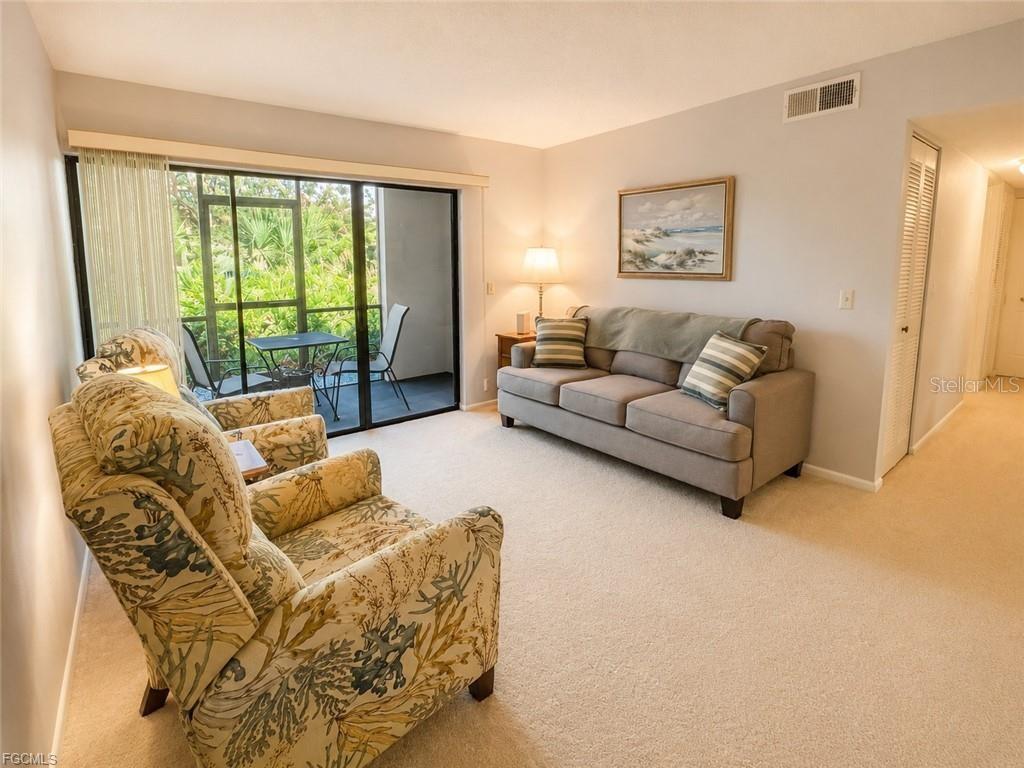 A living room features a sofa, patterned armchair, beige carpet, and a sliding glass door — 1515 FORREST NELSON BOULEVARD UNIT M106, PORT CHARLOTTE, FL