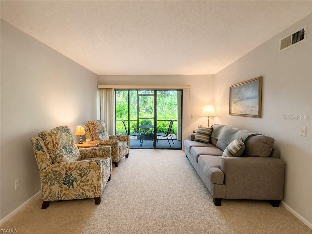 A living room features a gray sofa, two patterned armchairs, and a sliding glass door — 1515 FORREST NELSON BOULEVARD UNIT M106, PORT CHARLOTTE, FL