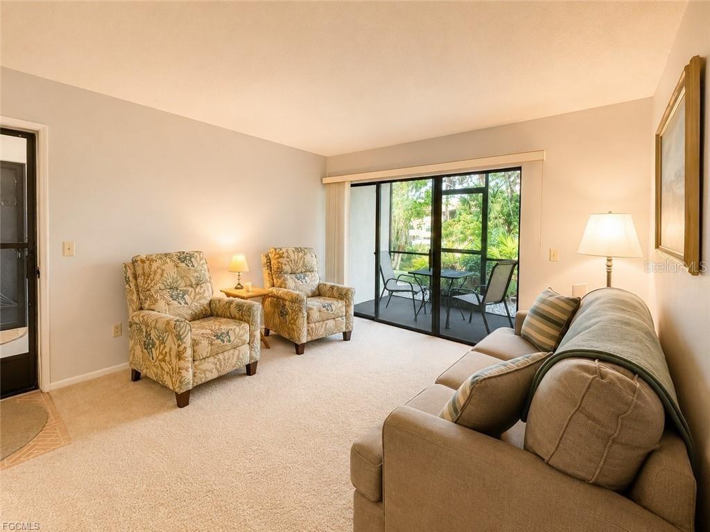 A living room features two floral armchairs, a sofa, and sliding glass doors to a balcony — 1515 FORREST NELSON BOULEVARD UNIT M106, PORT CHARLOTTE, FL