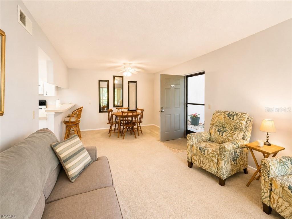 A living and dining area features beige carpeting, a grey sofa, and a floral armchair — 1515 FORREST NELSON BOULEVARD UNIT M106, PORT CHARLOTTE, FL