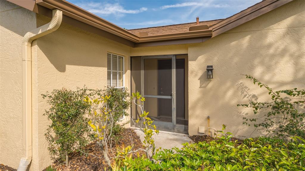 A tan stucco house exterior features a screened front door, a window, and landscaping — 5905 DORAL DRIVE, SARASOTA, FL