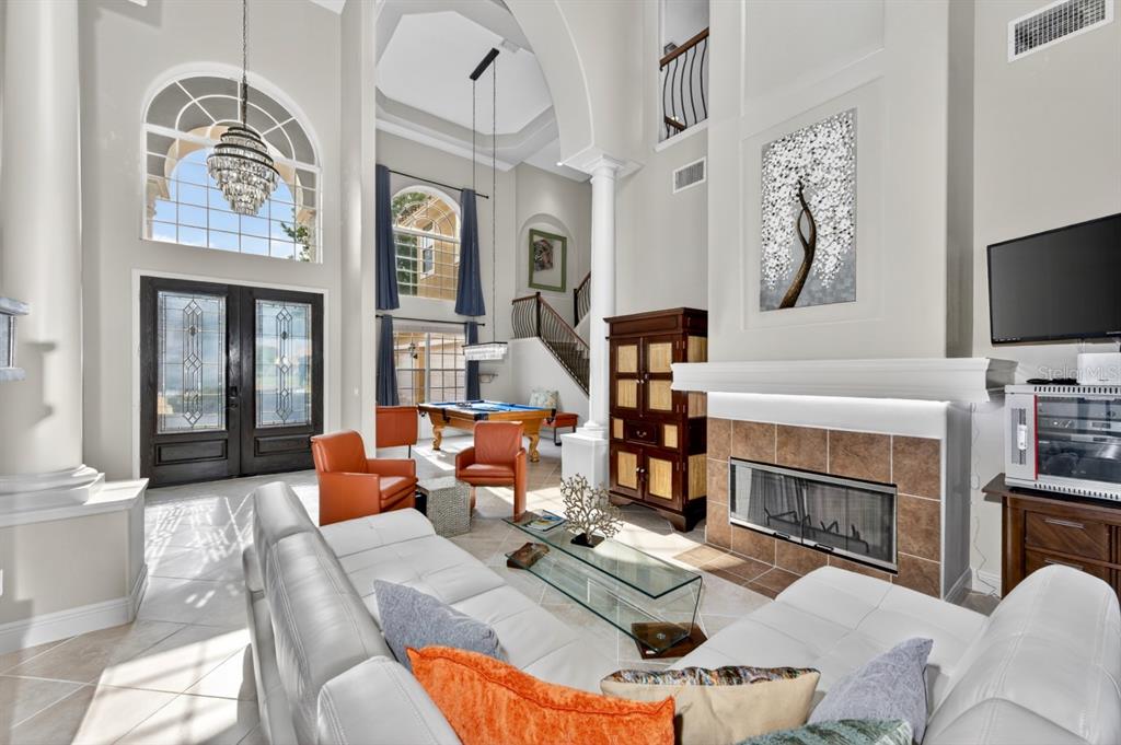 A high-ceilinged living room features a fireplace, white sofas, orange chairs, and a pool table — 2234 CALLAWAY COURT, DAVENPORT, FL