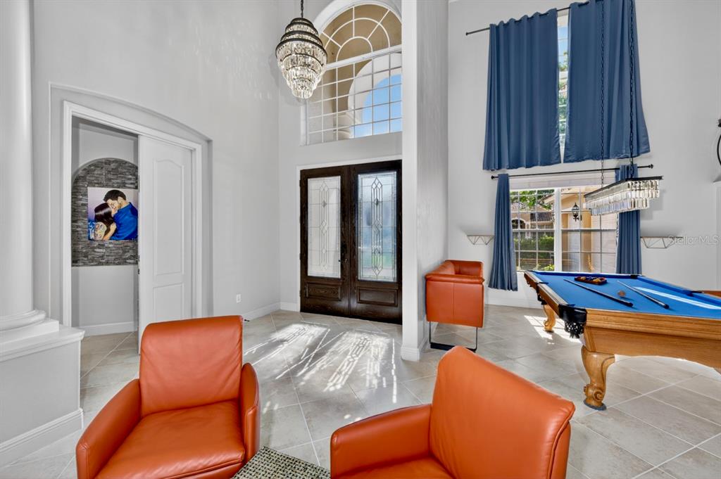 A high-ceilinged foyer features a pool table, orange leather chairs, and a crystal chandelier — 2234 CALLAWAY COURT, DAVENPORT, FL
