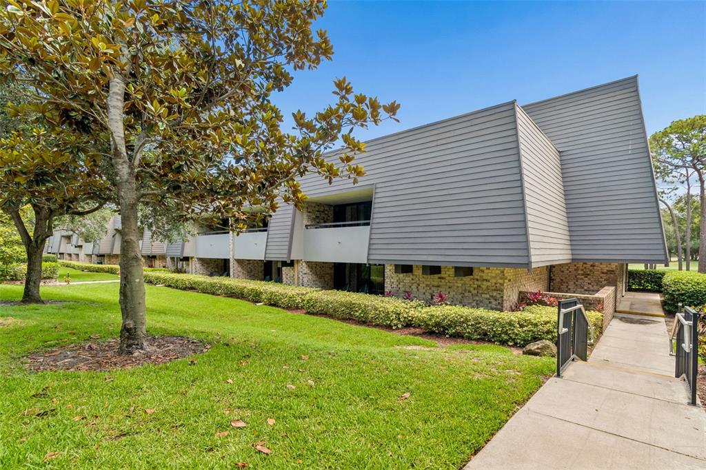 A multi-story building with gray horizontal siding and a brick base sits near a lawn — 36750 US HIGHWAY 19 UNIT 21202, PALM HARBOR, FL