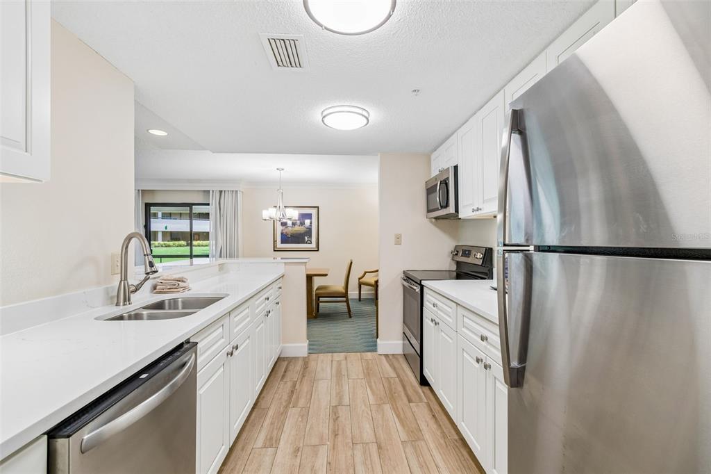 A kitchen with white cabinets, stainless steel appliances, and wood-look flooring opens to a dining area — 36750 US HIGHWAY 19 UNIT 21202, PALM HARBOR, FL