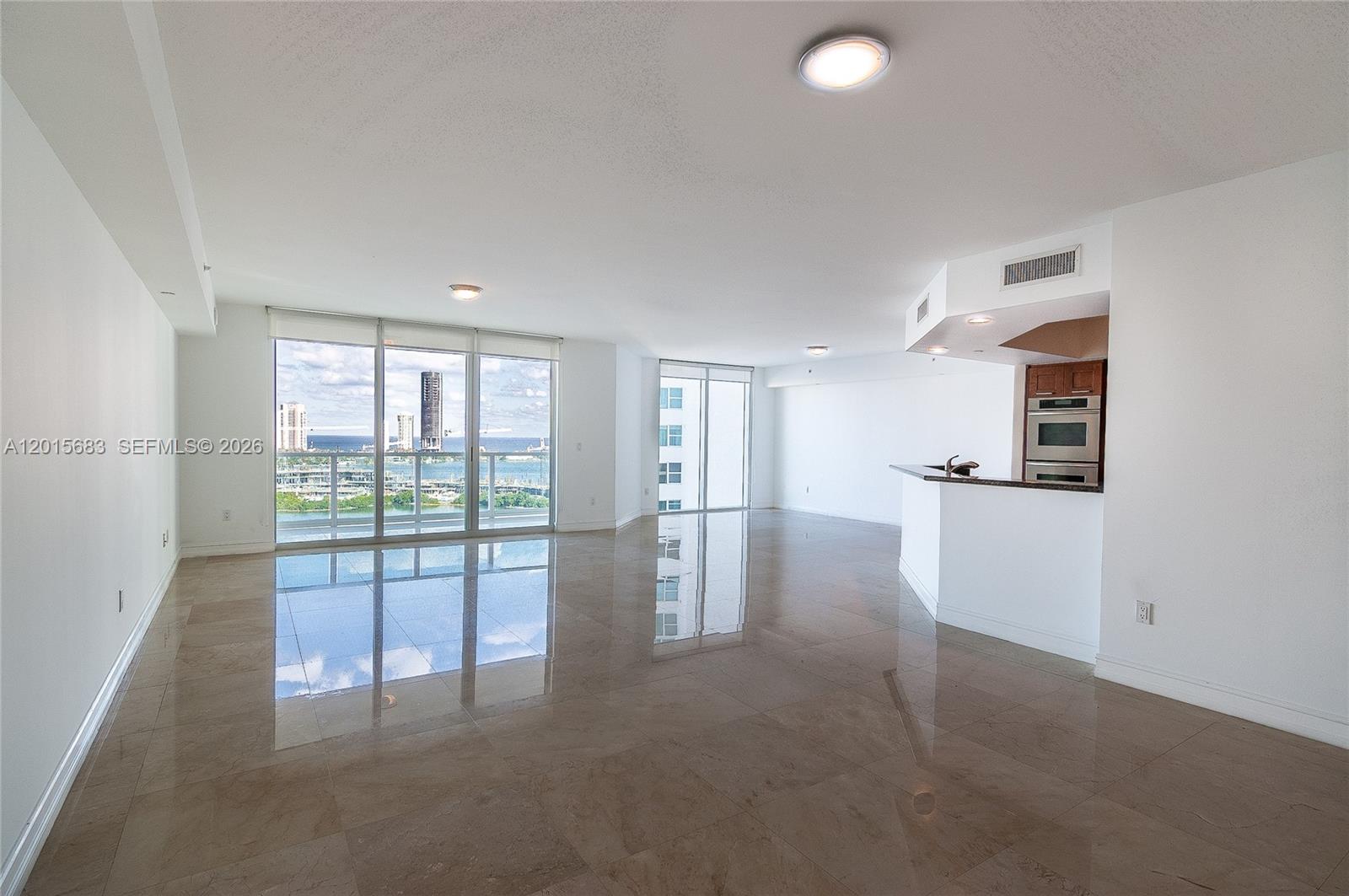 A bright, open-concept living area features polished tile floors, a kitchen peninsula, and floor-to-ceiling windows — AVENTURA, FL