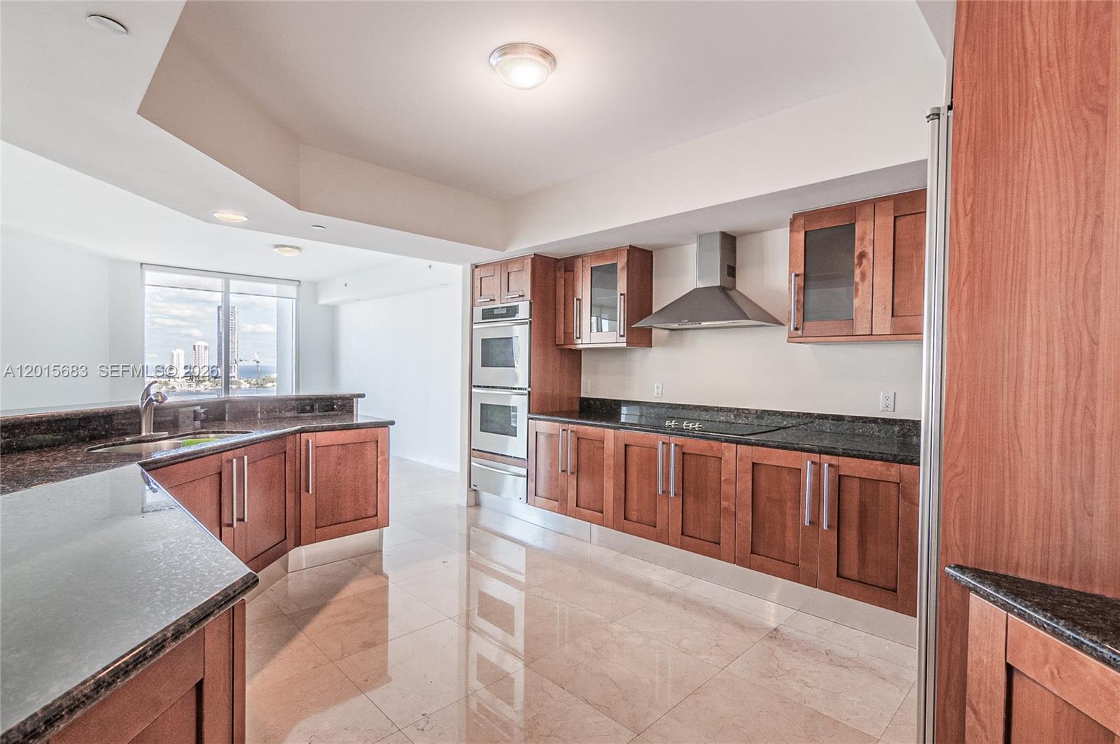 A kitchen features wood cabinets, dark granite countertops, stainless steel appliances, and tile flooring — AVENTURA, FL