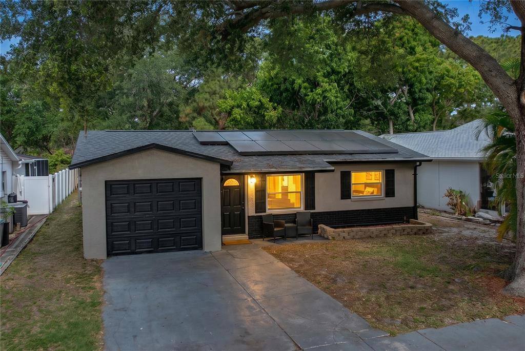 A single-story house with a gray exterior, black garage door, and solar panels on the roof — 8320 43RD WAY N, PINELLAS PARK, FL