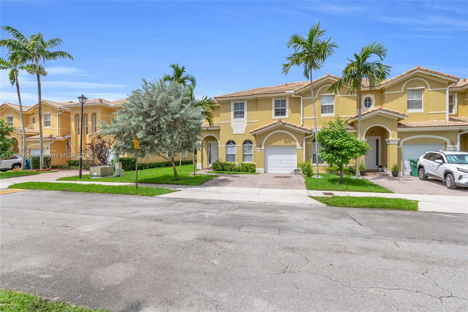 A street-level view of two-story yellow townhouses with palm trees and a paved driveway — 11742 SW 137th Pl, Miami FL 33186, MIAMI, FL
