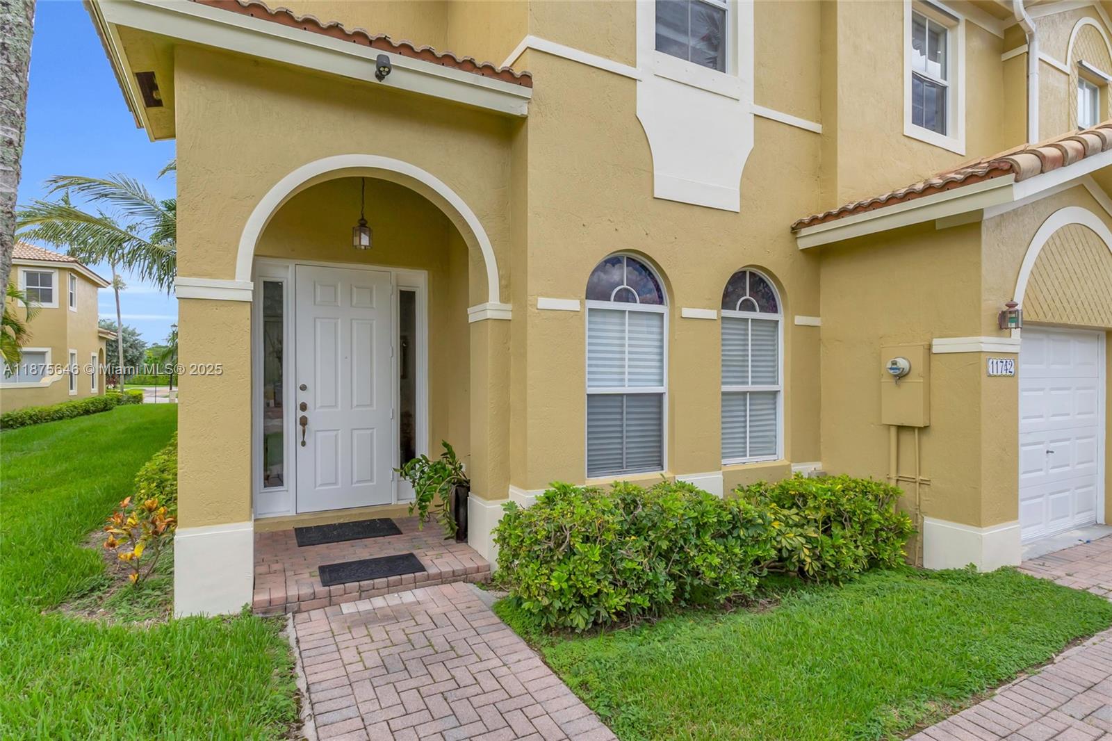 The exterior of a yellow two-story house features an arched entryway and a garage — 11742 SW 137th Pl, Miami FL 33186, MIAMI, FL
