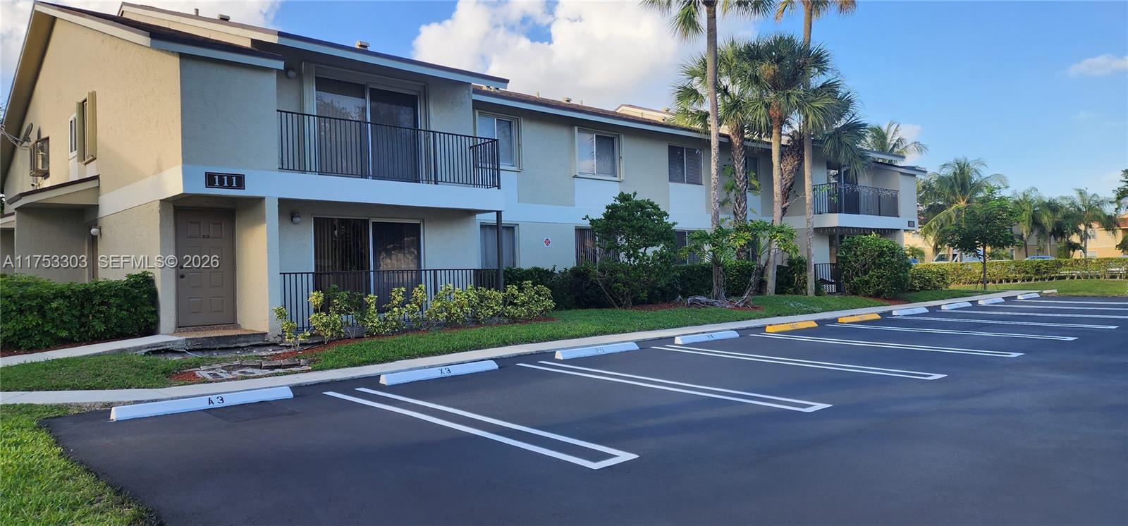 A two-story apartment building features a tan exterior, balconies, and a paved parking lot — 111 Gardens Dr # 203, Pompano Beach FL 33069, POMPANO BEACH, FL