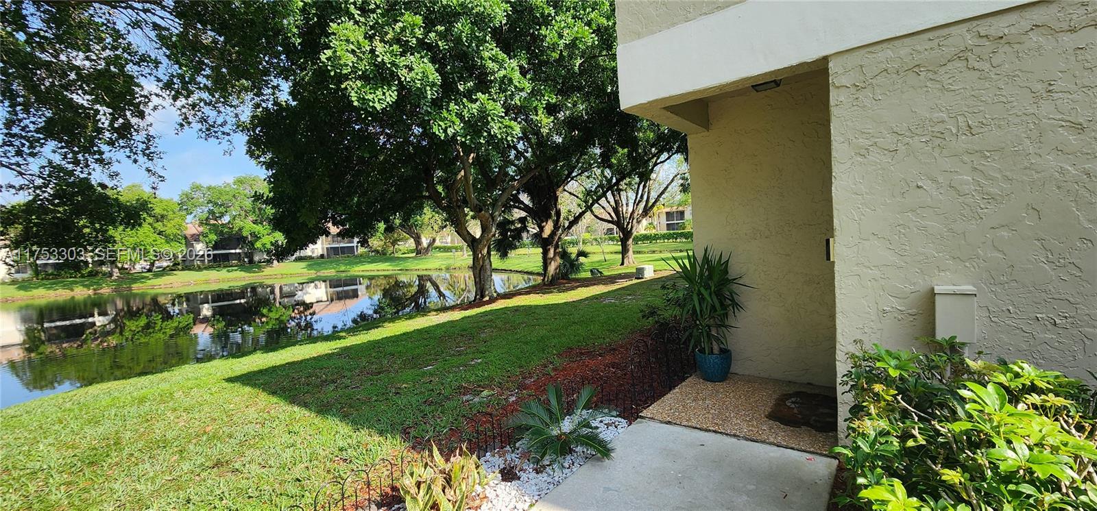 A view of a grassy yard and a pond from a building's concrete entryway — 111 Gardens Dr # 203, Pompano Beach FL 33069, POMPANO BEACH, FL