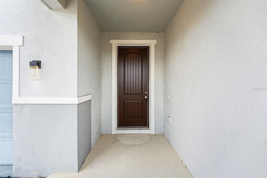 A covered entryway features a brown front door and a light fixture on the wall — 2312 BISCOTTO CIRCLE, DAVENPORT, FL