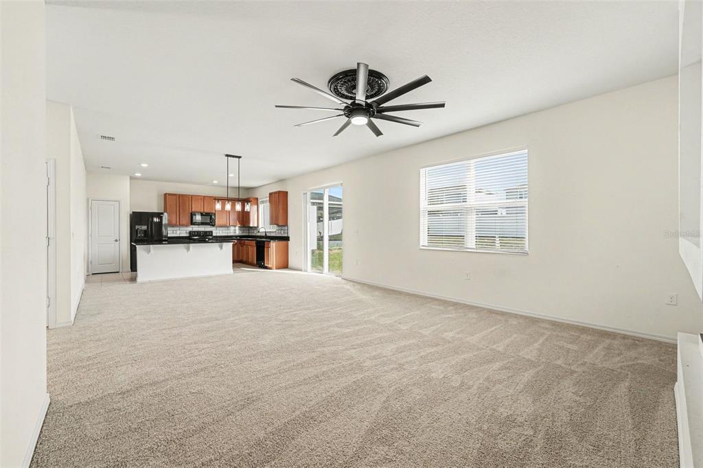 A carpeted living room opens to a kitchen with wooden cabinets and a ceiling fan — 2312 BISCOTTO CIRCLE, DAVENPORT, FL