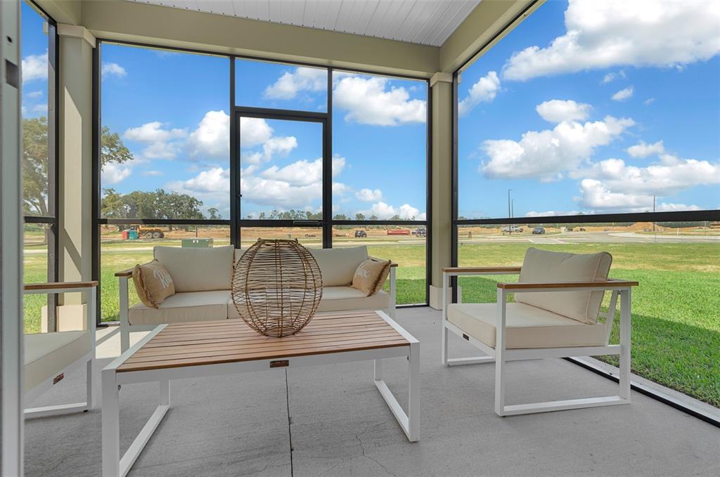 A screened-in patio features modern white furniture and a view of an undeveloped field — 8700 SW 67TH CIRCLE, OCALA, FL