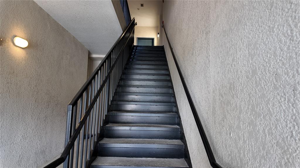 A straight staircase with black metal railings leads up to a landing with a doorway — 3051 GREYSTONE LOOP UNIT 206, KISSIMMEE, FL