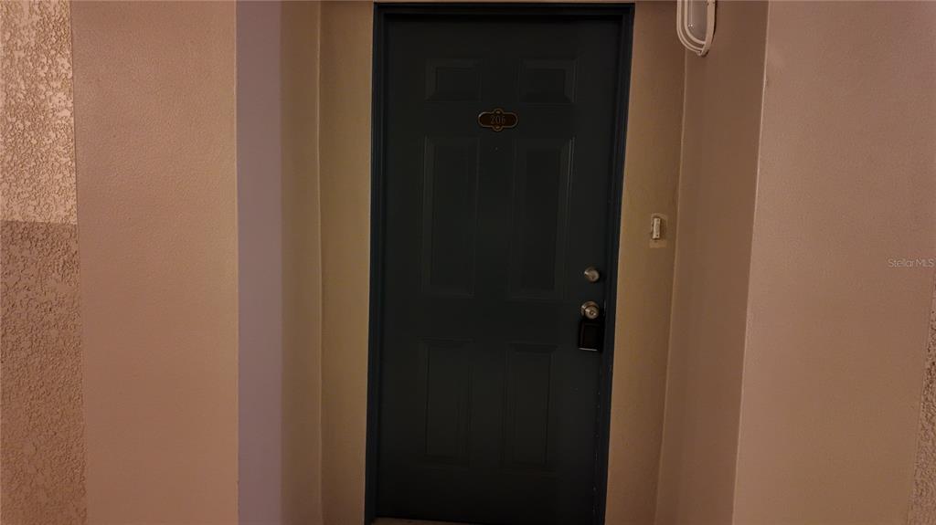 A dark blue front door with a number plate is set within a beige hallway — 3051 GREYSTONE LOOP UNIT 206, KISSIMMEE, FL