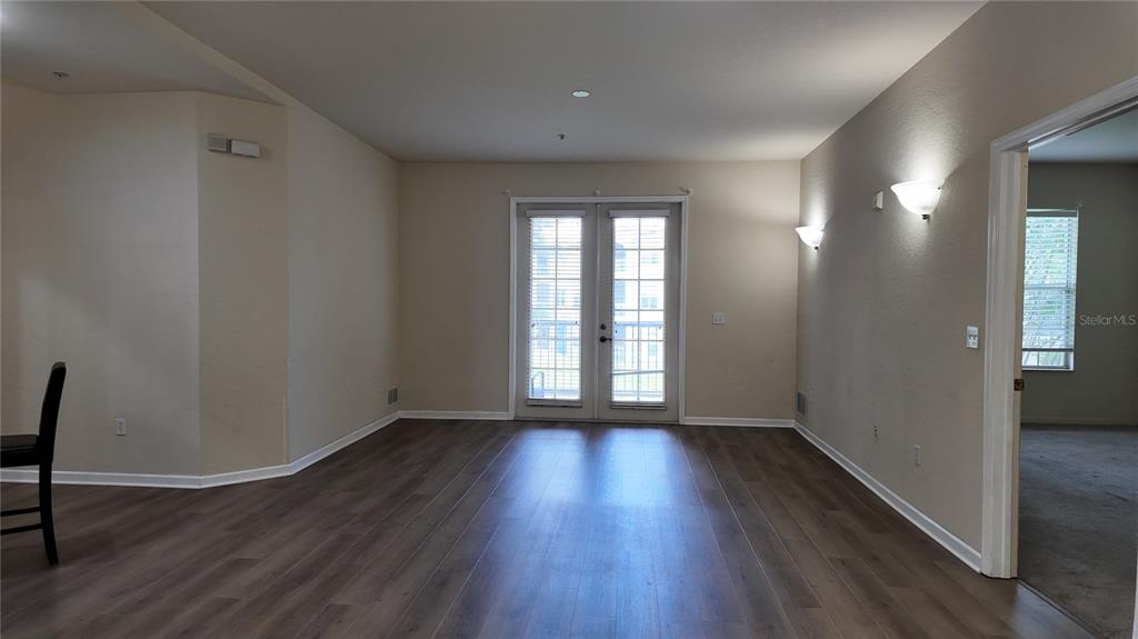 An empty room features wood-look flooring, beige walls, and glass double doors leading outside — 3051 GREYSTONE LOOP UNIT 206, KISSIMMEE, FL