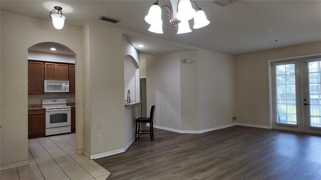A kitchen with wood cabinets and tile floors opens to a living area with wood flooring — 3051 GREYSTONE LOOP UNIT 206, KISSIMMEE, FL