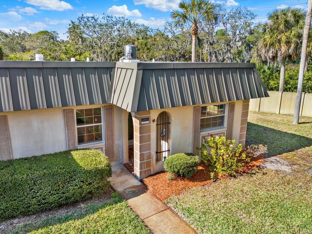 An exterior view of a single-story home with a metal mansard roof and landscaping — 4455 RUSTIC DRIVE, NEW PORT RICHEY, FL