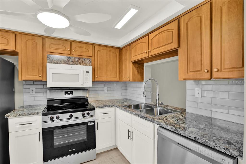 A kitchen features wood upper cabinets, white lower cabinets, granite countertops, and stainless steel appliances — 4455 RUSTIC DRIVE, NEW PORT RICHEY, FL