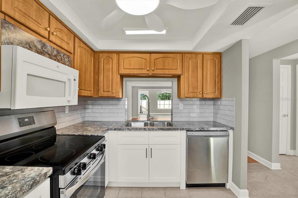 A kitchen features wood upper cabinets, white lower cabinets, stainless steel appliances, and granite countertops — 4455 RUSTIC DRIVE, NEW PORT RICHEY, FL