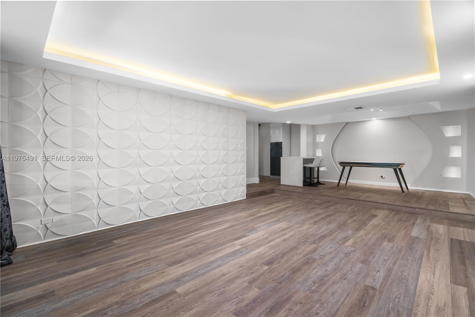 A modern room features a textured accent wall, wood-look flooring, and a raised platform area — 3730 Inverrary Dr # 2H, Lauderhill FL 33319, LAUDERHILL, FL