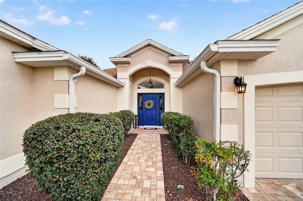 A paved walkway leads to the blue front door of a beige house with landscaping — 8293 SE 176TH LAWSON LOOP, THE VILLAGES, FL
