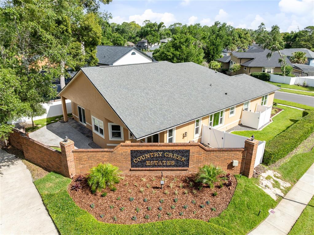 An aerial view shows a tan house behind a brick Country Creek Estates entrance sign — 683 OAK HOLLOW WAY, ALTAMONTE SPRINGS, FL