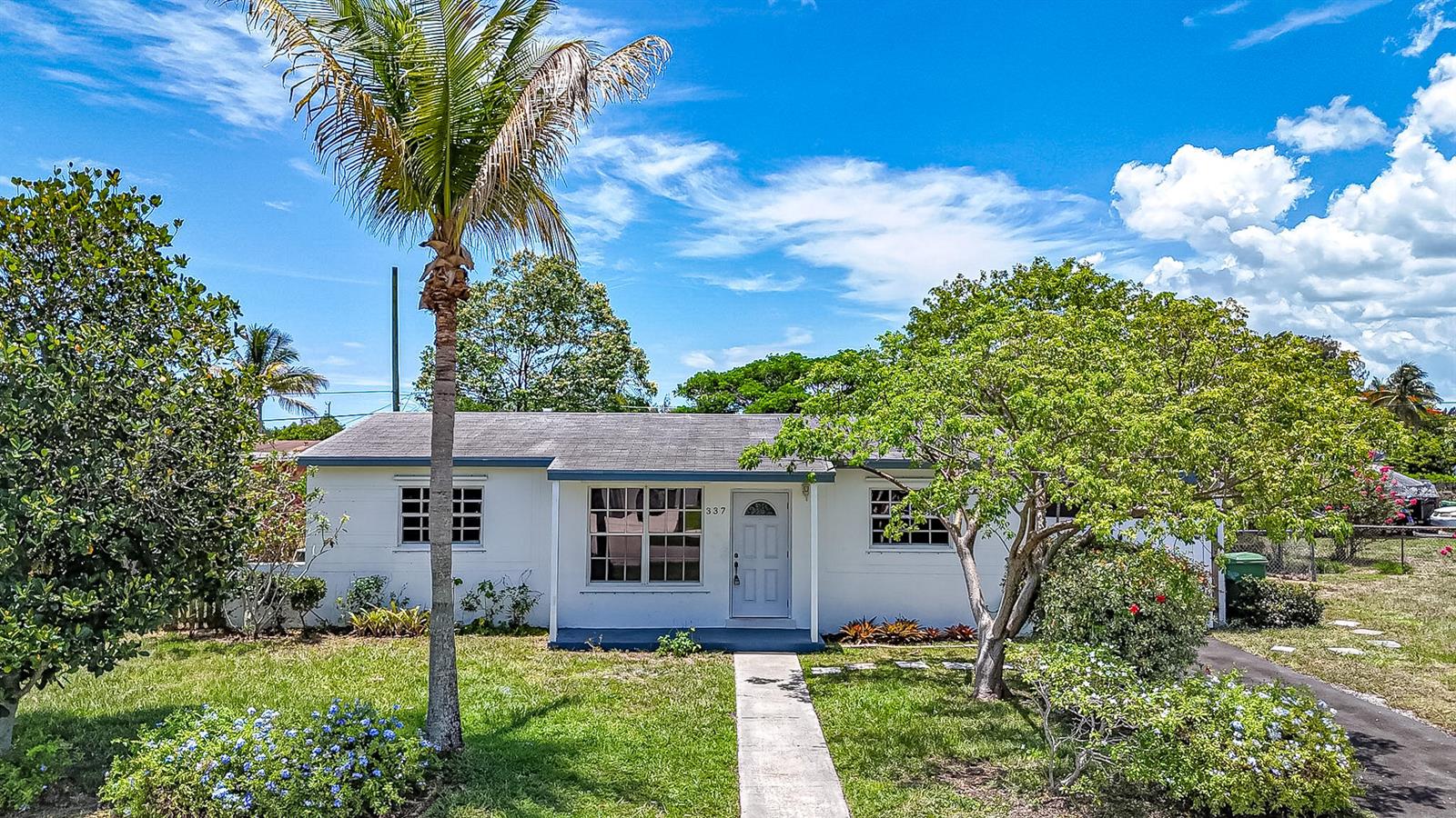 A single-story white house with a palm tree and a front walkway under a blue sky — 337 Mid Pines Road, Palm Springs FL 33461, PALM SPRINGS, FL