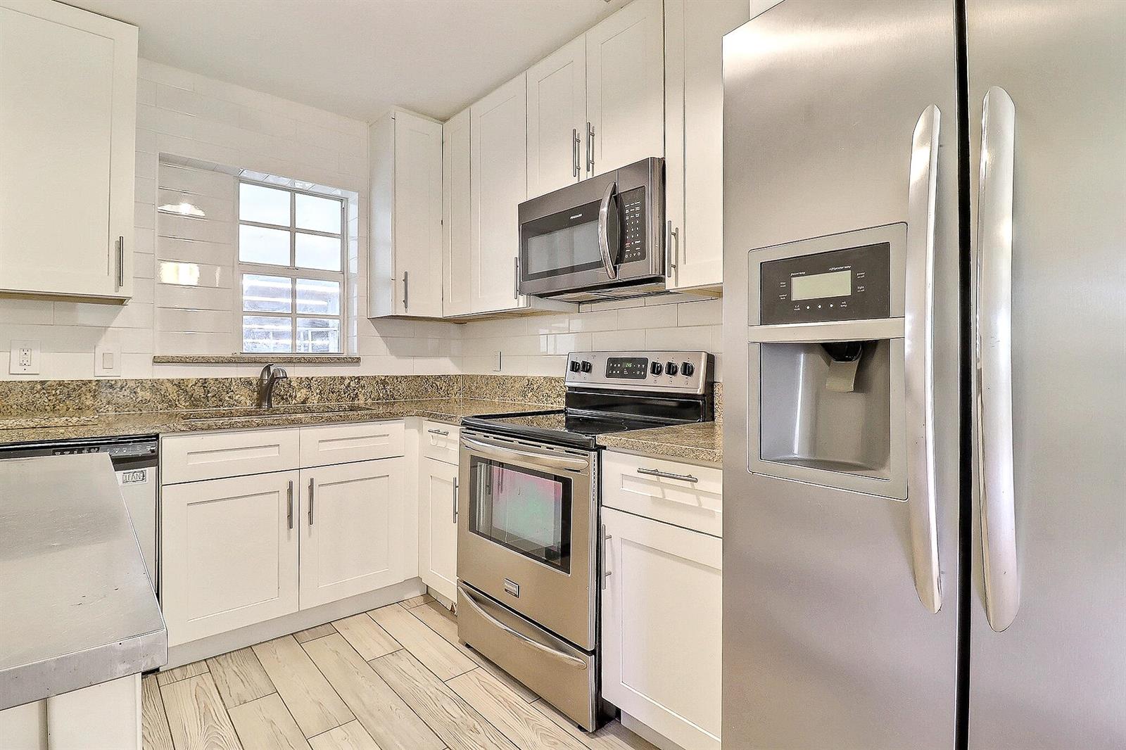 A kitchen features white cabinets, stainless steel appliances, granite countertops, and light wood-look tile flooring — 337 Mid Pines Road, Palm Springs FL 33461, PALM SPRINGS, FL