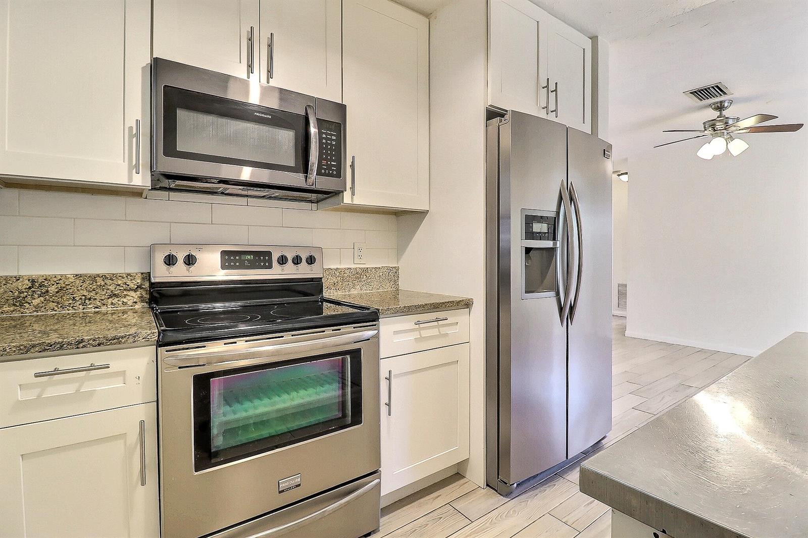 A kitchen features white cabinets, stainless steel appliances, and granite countertops — 337 Mid Pines Road, Palm Springs FL 33461, PALM SPRINGS, FL