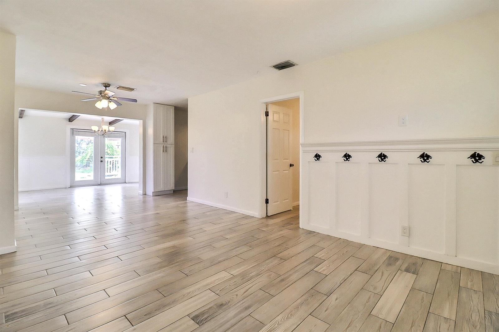 A bright living area features wood-look tile flooring, white wainscoting with hooks, and a doorway — 337 Mid Pines Road, Palm Springs FL 33461, PALM SPRINGS, FL