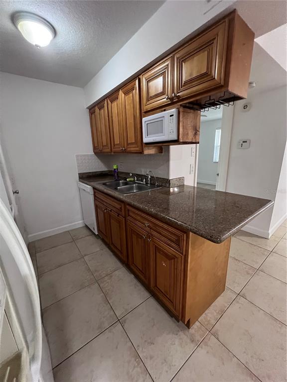 A kitchen features wood cabinets, a granite countertop, a stainless steel sink, and tile flooring — 226 THORN TREE PLACE UNIT 226, BRANDON, FL