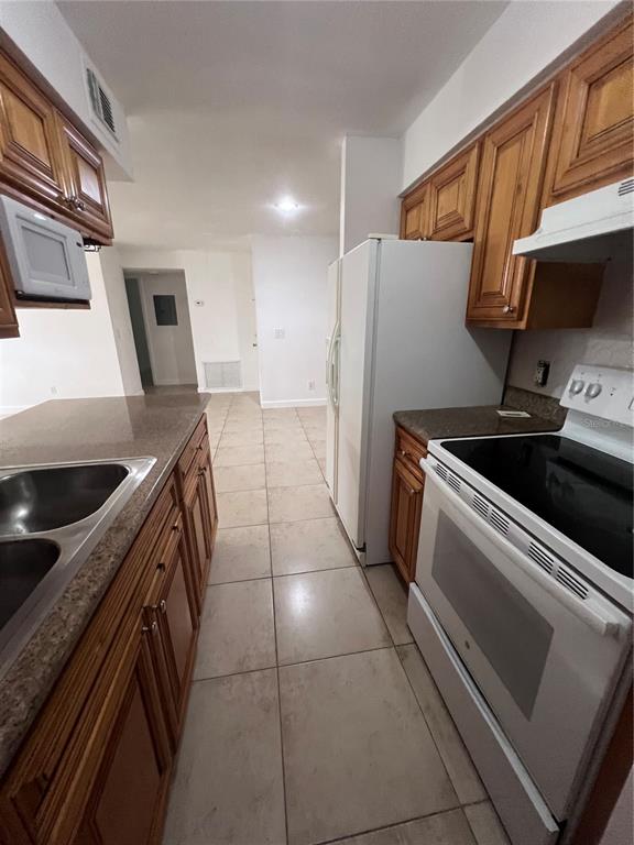 A kitchen features wood cabinets, granite countertops, tile flooring, and white appliances — 226 THORN TREE PLACE UNIT 226, BRANDON, FL