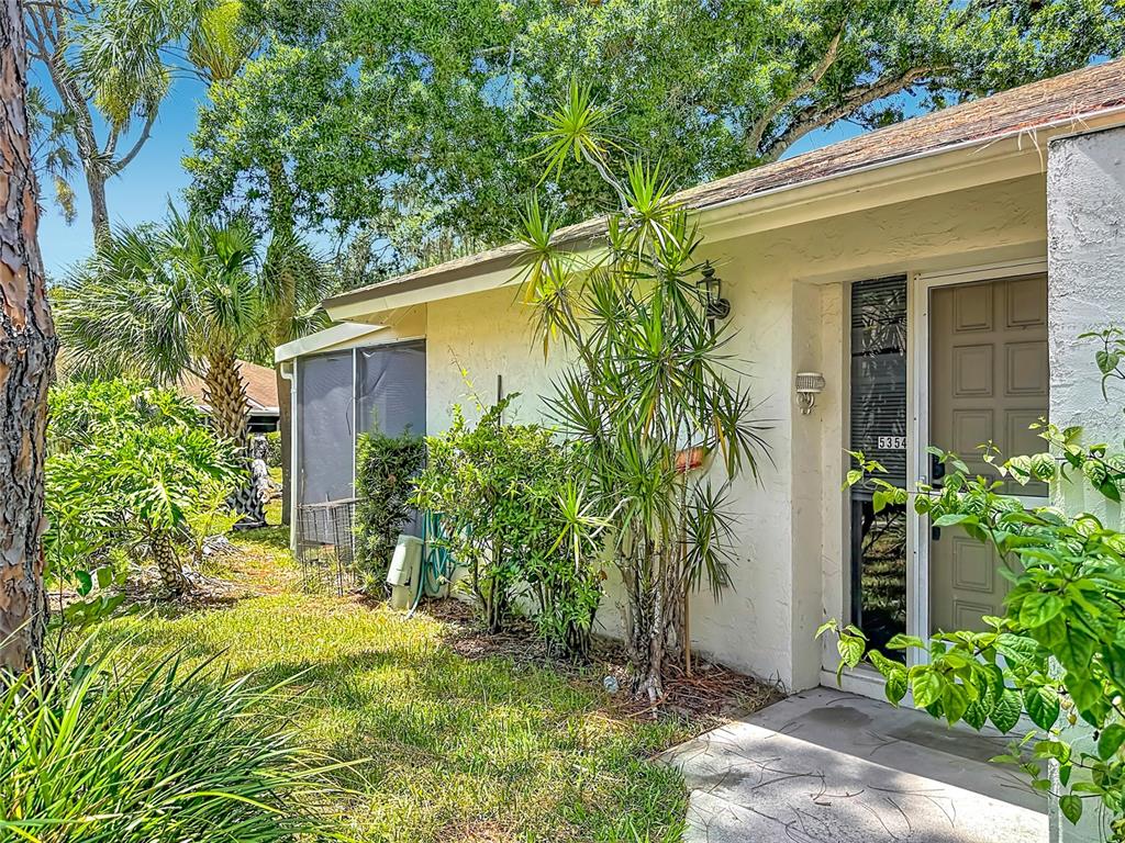 A view of a home exterior with a tan stucco wall, front door, and landscaping — 5354 ROYAL PALM AVENUE UNIT 5354, SARASOTA, FL