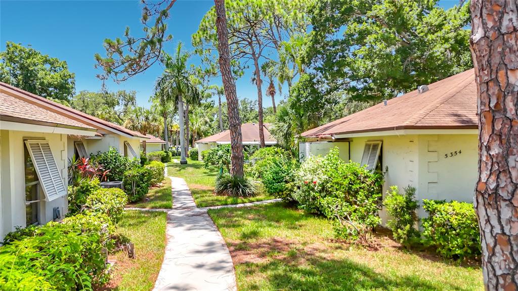 A paved walkway leads between two single-story residential buildings surrounded by trees and landscaping — 5354 ROYAL PALM AVENUE UNIT 5354, SARASOTA, FL