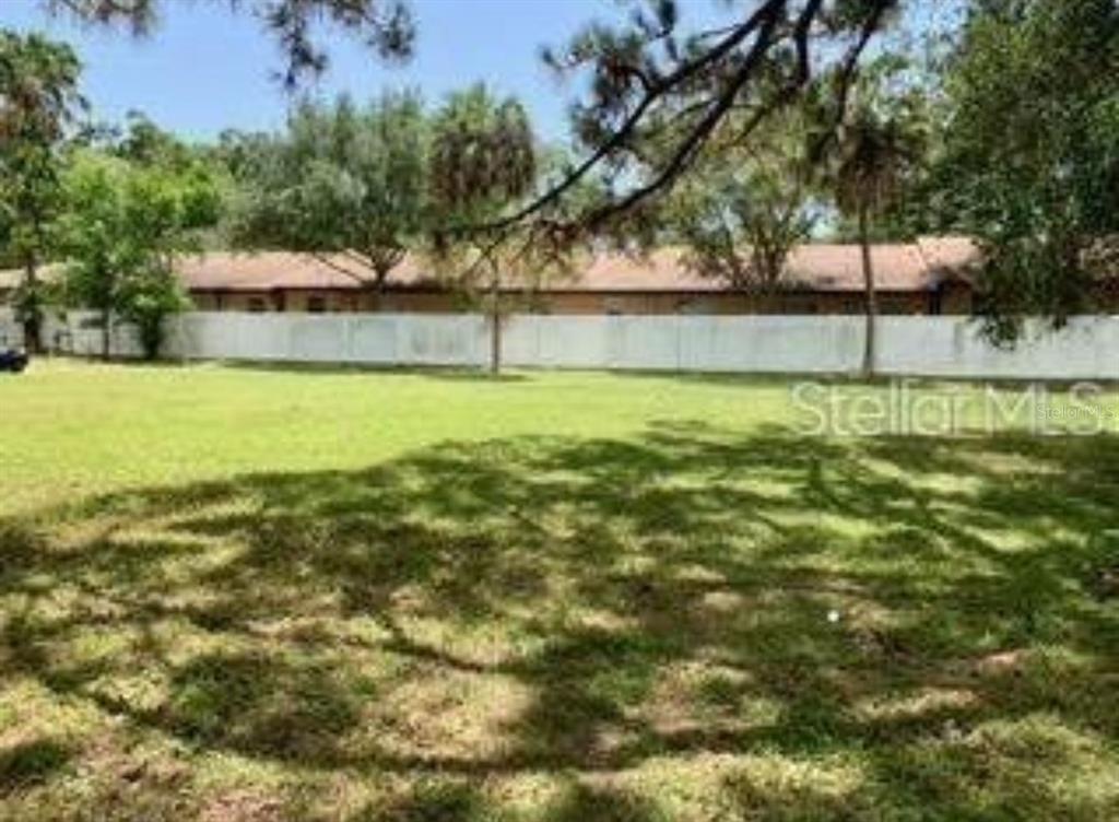 A grassy backyard features a white vinyl fence and mature trees under a bright sky — 22ND AVENUE S, ST PETERSBURG, FL