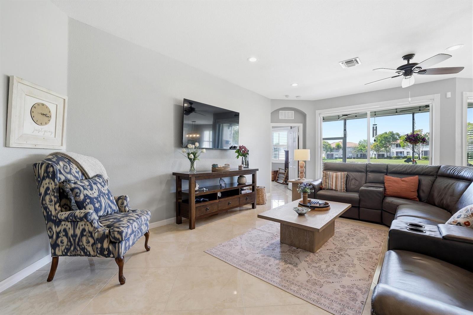 A living room features a dark leather sectional, patterned armchair, wood console, and tile flooring — 2101 Wingate Bend, Wellington FL 33414, WELLINGTON, FL