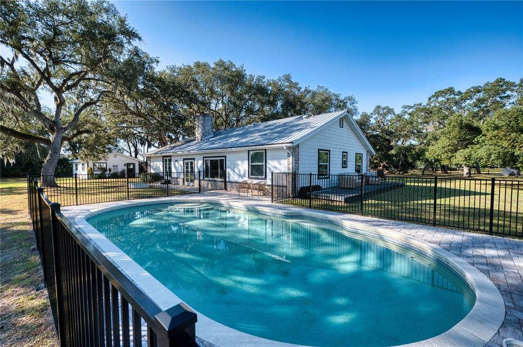 A white house with a metal roof sits behind a fenced-in oval swimming pool — 5310 JIM DAVIS ROAD, PARRISH, FL